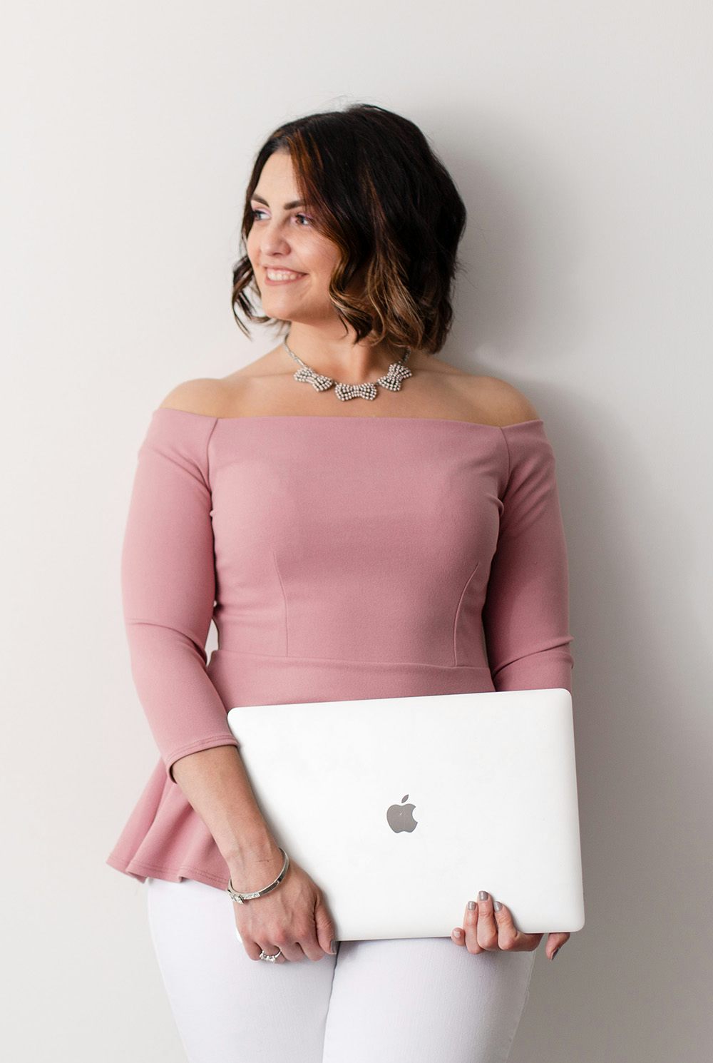 Smiling white woman with a curled brown bob looking off camera to the left, holding a Macbook Pro