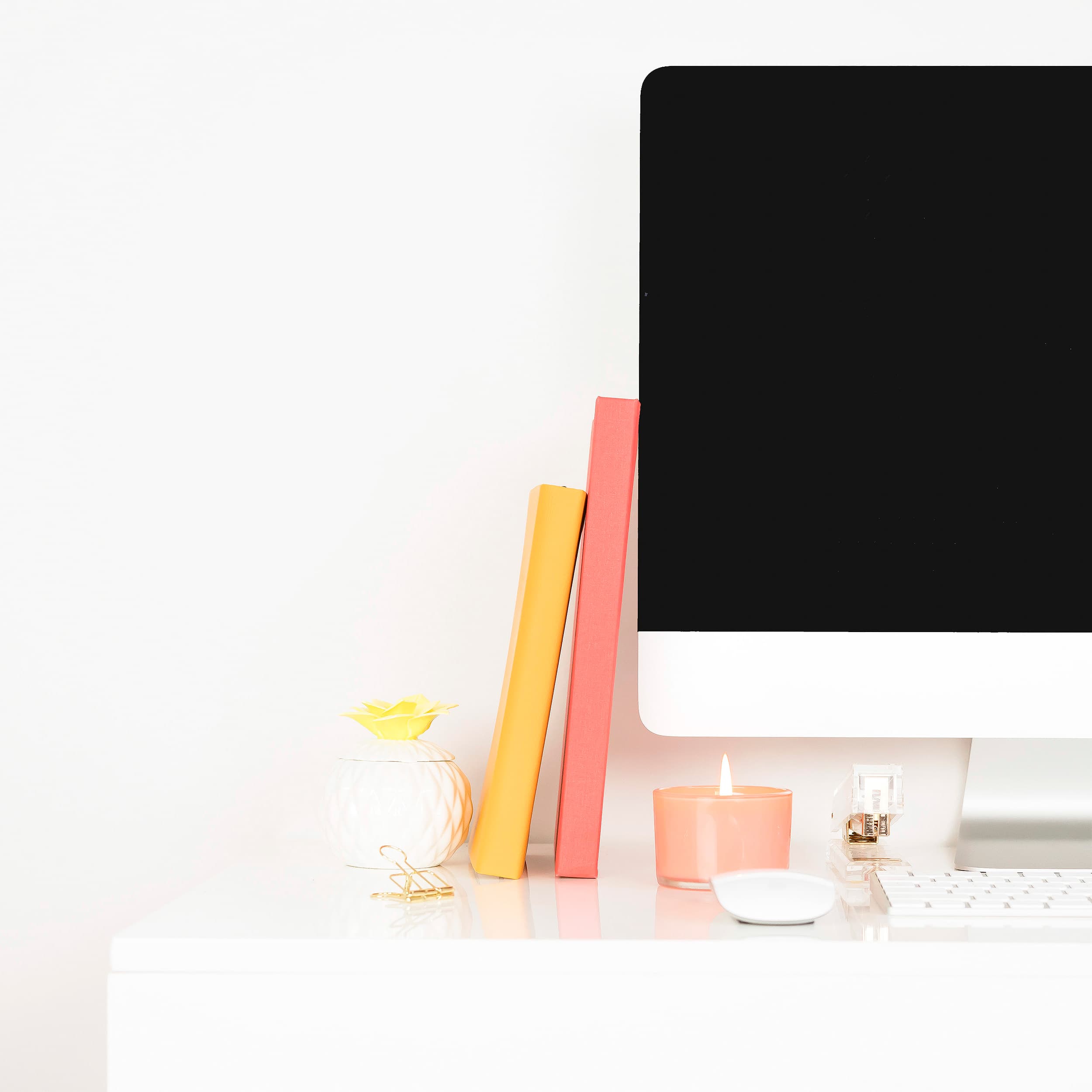 White desk with iMac, yellow and pink notebooks, and a candle