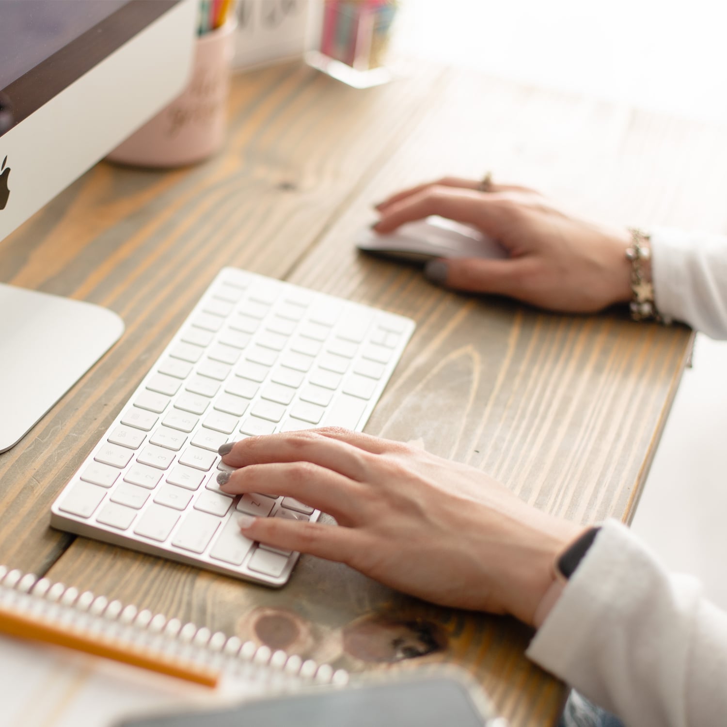 Hands with manicured nails typing on iMac keyboard