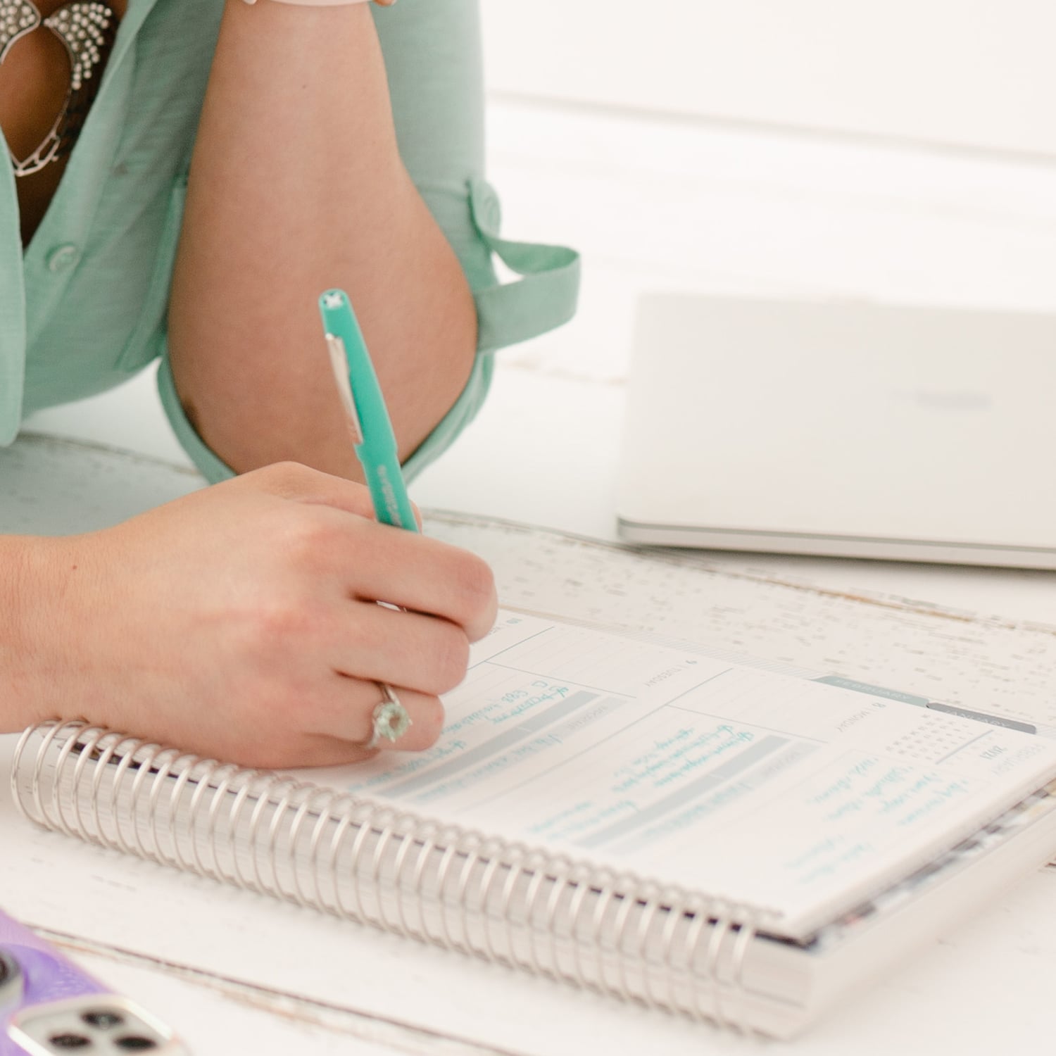 Closeup on hands while Megan is writing in a notebook with a teal pen