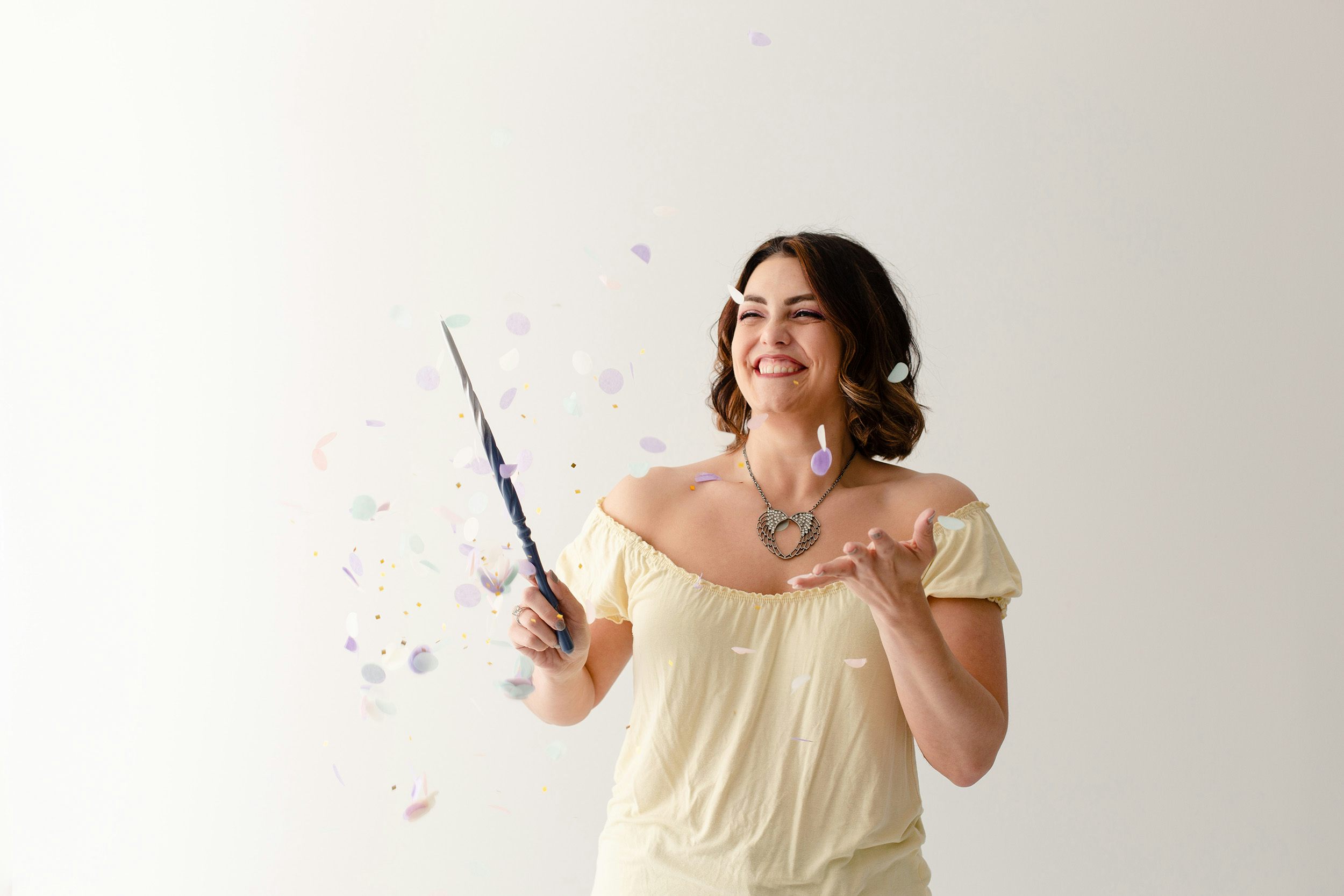 Megan laughing as she waves her magic wand, surrounded by confetti and sparkles